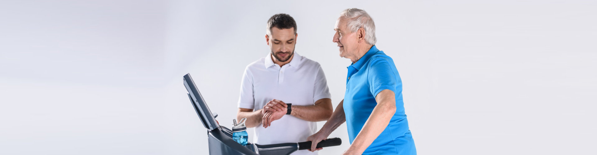 therapist checking time while assisting senior men exercising on treadmill